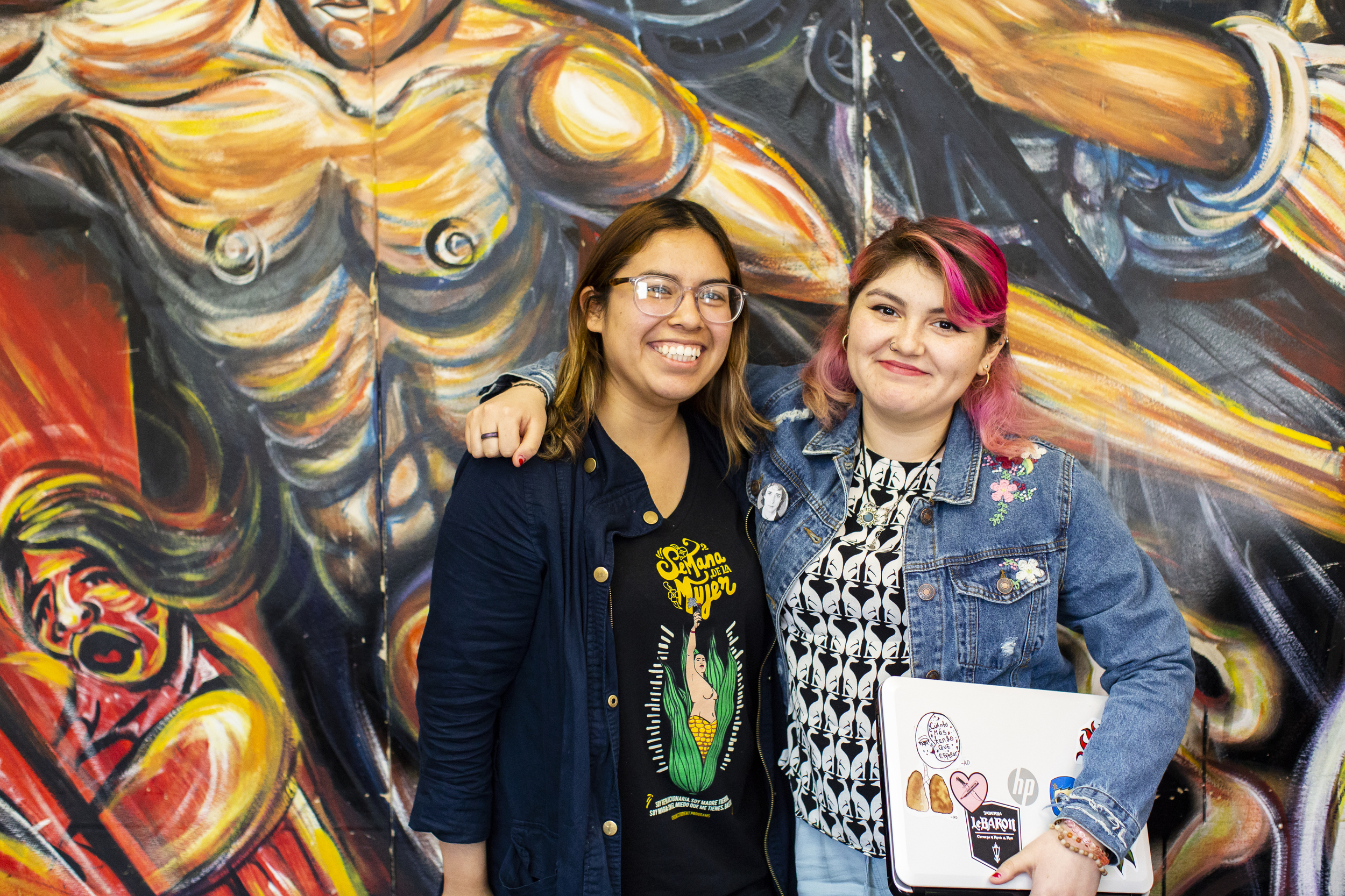 Two students in front of a colorfully painted wall